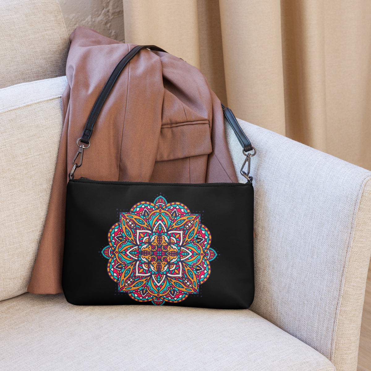 A black crossbody bag with a colorful mandala print,of Exclusivestan styled on a beige armchair with a brown jacket draped over it.